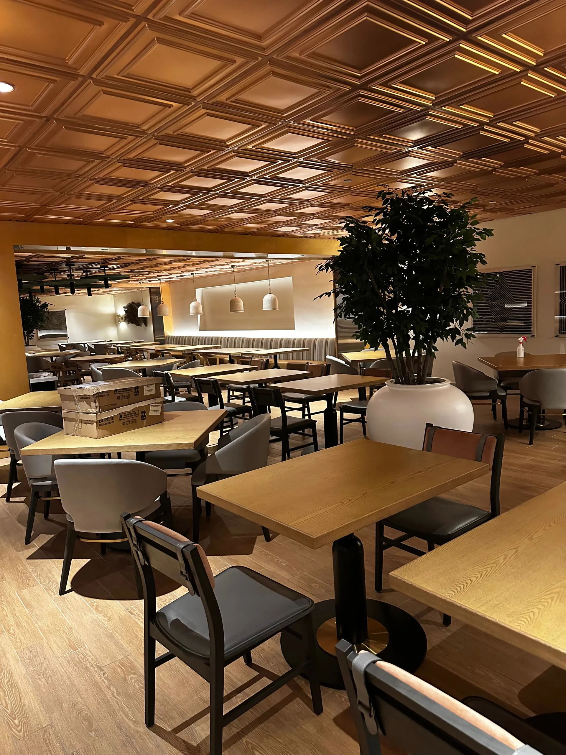 Dining room with a warm-toned coffered ceiling, tables, and banquette seating along the back wall.